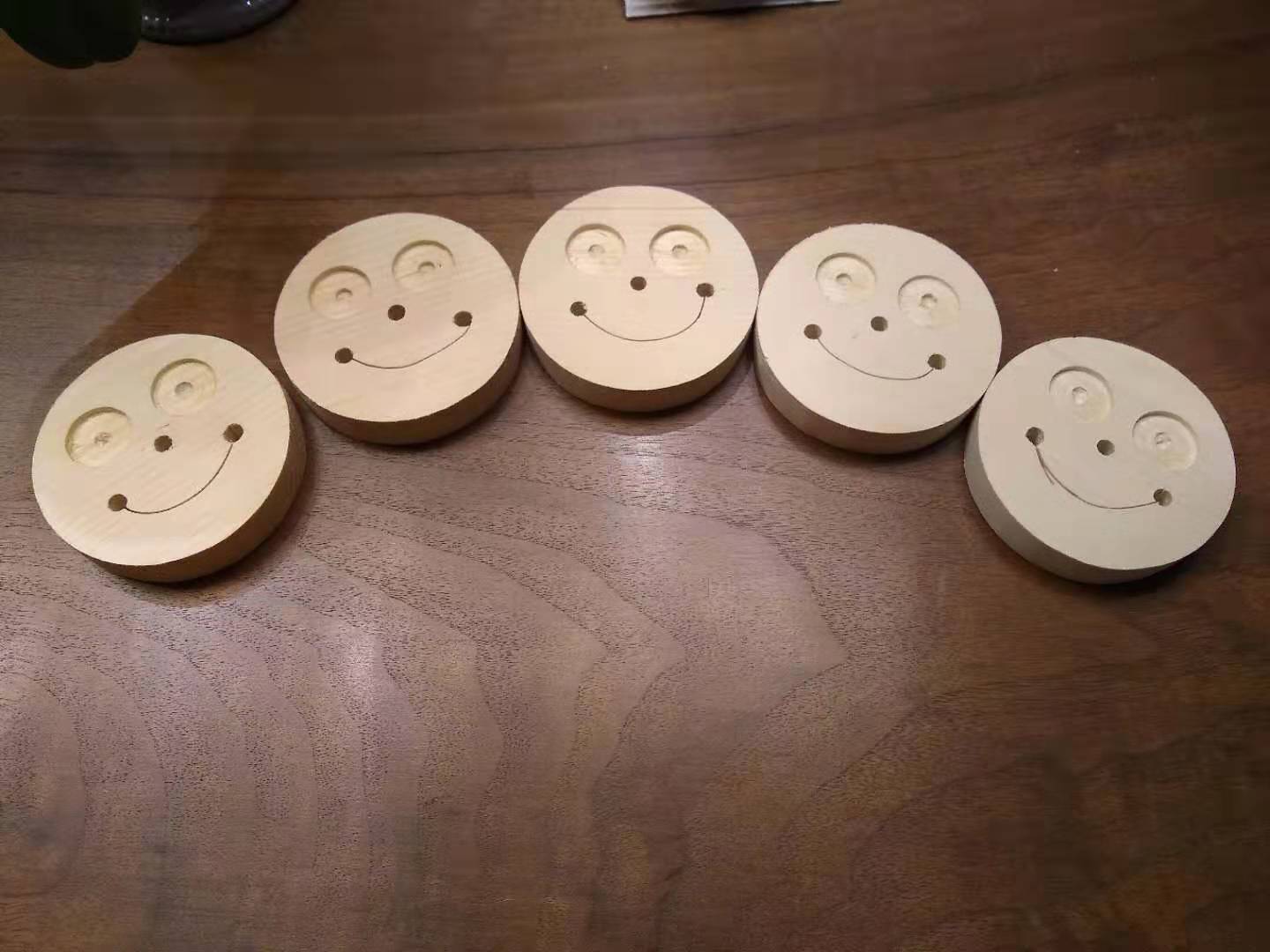 A picture of five small smiling faces made of wood, lined up on a table.